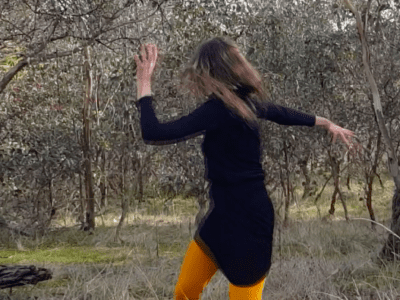A woman mid movement, hair and arms flaring, dancing in the bush.